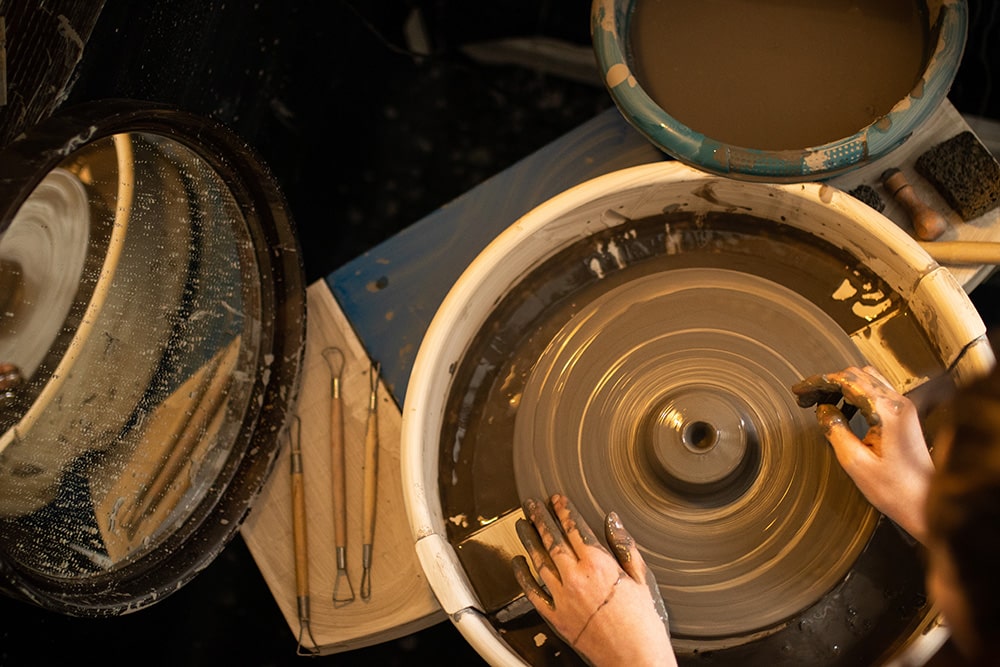 Les mains de Manon Renault, céramiste près de Doué en Anjou et Saumur, en train de confectionner ses pièces en céramique artisanale sur un tour, photographiée dans son atelier par Margot Vincent alias Margotine Photographies, photographe près d'Angers dans le maine-et-loire