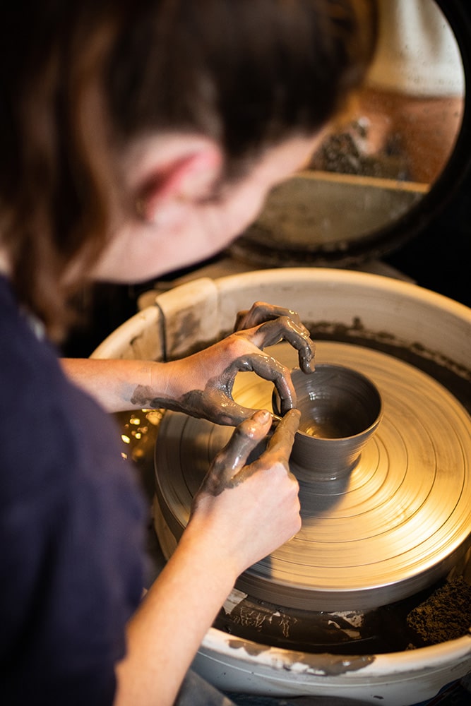 Les mains de Manon Renault, céramiste près de Doué en Anjou et Saumur, en train de confectionner ses pièces en céramique artisanale sur un tour, photographiée dans son atelier par Margot Vincent alias Margotine Photographies, photographe près d'Angers dans le maine-et-loire