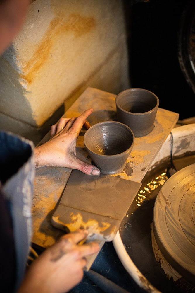 Les mains de Manon Renault, céramiste près de Doué en Anjou et Saumur, en train de déplacer délicatement ses pièces en céramique artisanale, photographiée dans son atelier par Margot Vincent alias Margotine Photographies, photographe près d'Angers dans le maine-et-loire