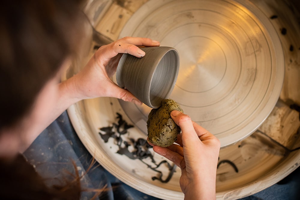 Les mains de Manon Renault, céramiste près de Doué en Anjou et Saumur, en train de confectionner ses pièces en céramique artisanale sur un tour, photographiée dans son atelier par Margot Vincent alias Margotine Photographies, photographe près d'Angers dans le maine-et-loire