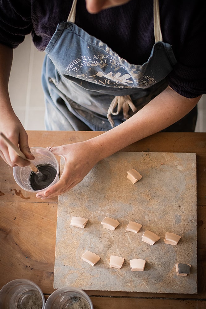 Essai et recherche de recette sur des fragments de poterie pour la confection d'un émail artisanal et naturel à base d'ardoise pour la céramique réalisée par Manon Renault, céramiste près de Doué en Anjou et Saumur photographié dans son atelier par Margot Vincent alias Margotine Photographies, photographe près d'Angers dans le maine-et-loire