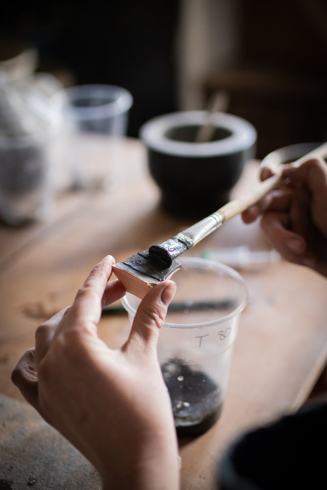 Essai et recherche de recette sur des fragments de poterie pour la confection d'un émail artisanal et naturel à base d'ardoise pour la céramique réalisée par Manon Renault, céramiste près de Doué en Anjou et Saumur photographié dans son atelier par Margot Vincent alias Margotine Photographies, photographe près d'Angers dans le maine-et-loire